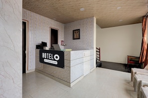 Un mostrador de recepción de hotel con un cartel que indica servicio de empresa, un cuadro enmarcado en la pared y una escalera que conduce a otra zona.