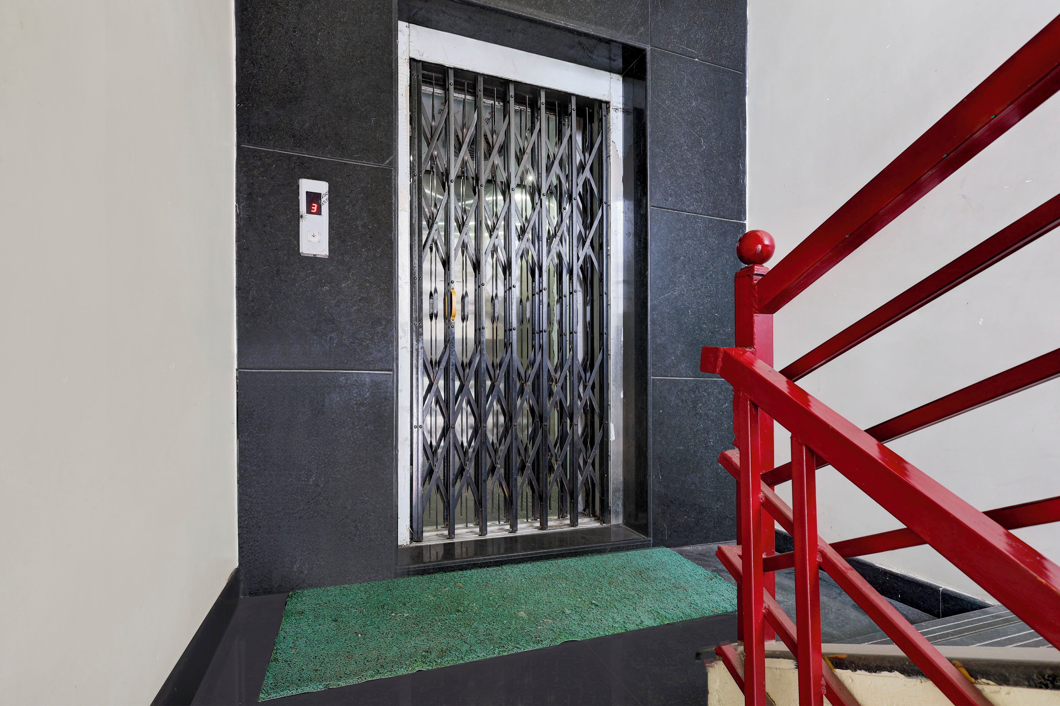 Un escalier avec des rampes rouges menant à une porte surmontée d’une grille de sécurité en métal.