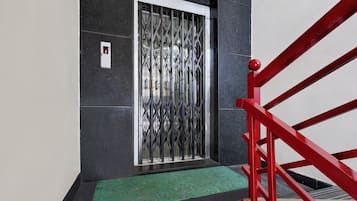 Un escalier avec des rampes rouges menant à une porte surmontée d’une grille de sécurité en métal.