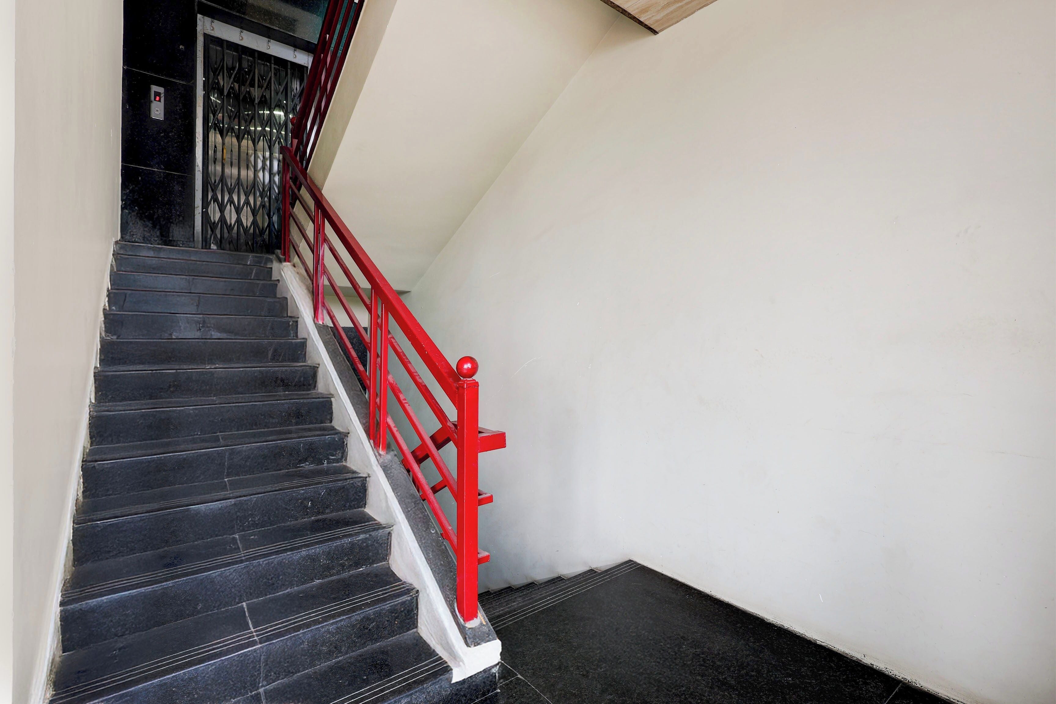 A staircase with black steps and a red handrail leading to a door with a metal gate.