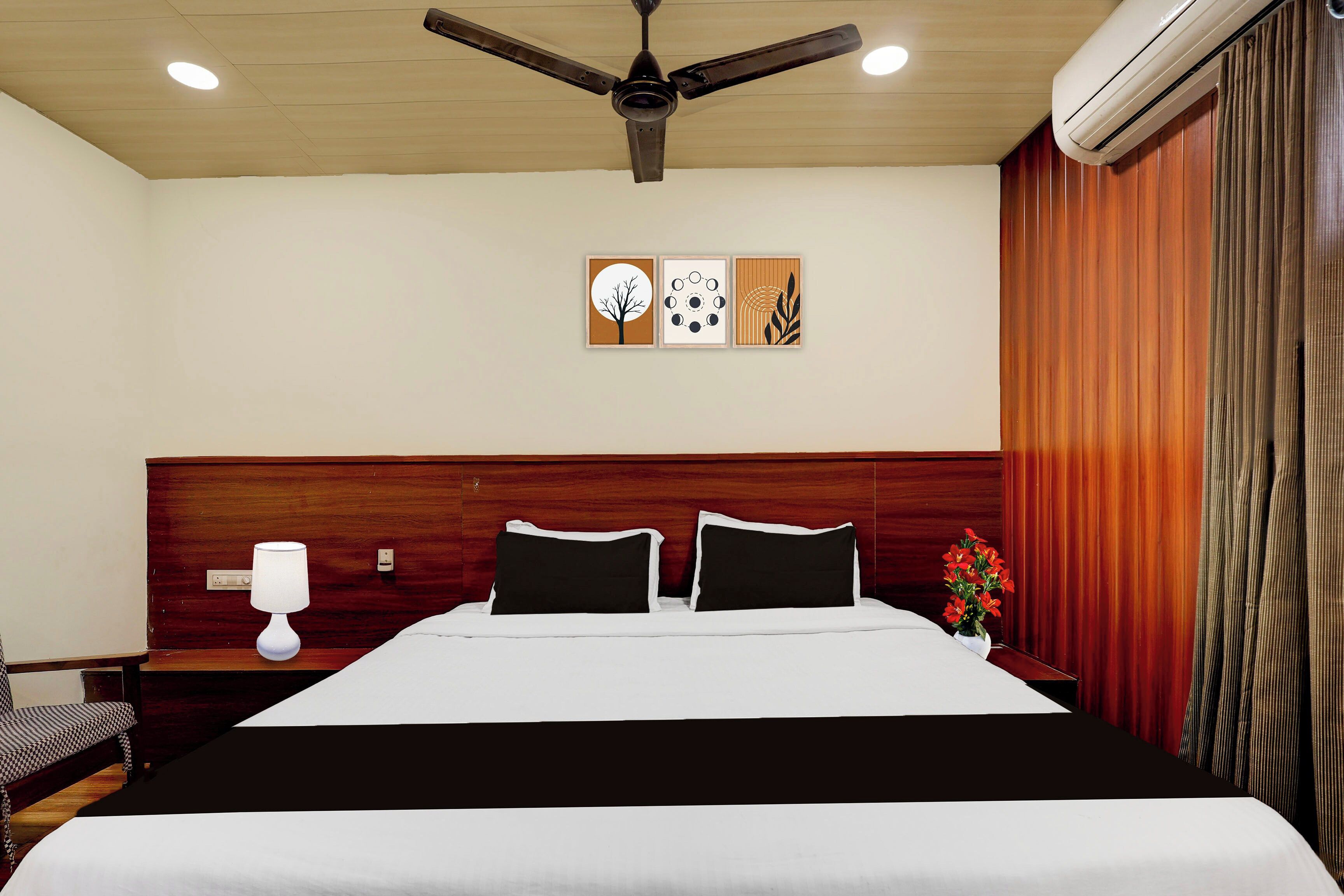 A hotel room with a bed, a nightstand, a lamp, a ceiling fan, and artwork on the wall.
