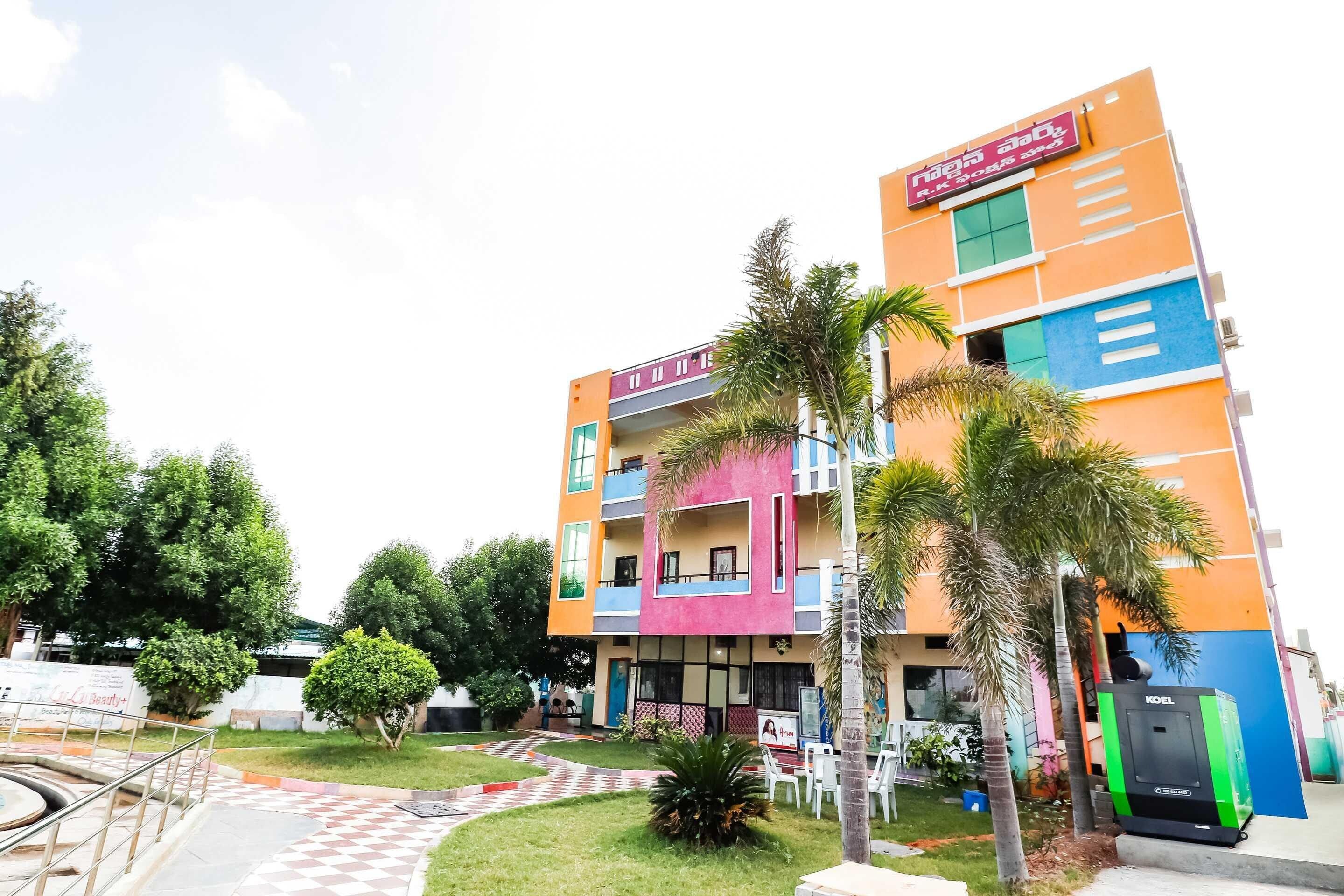 A multi-story building with a colorful facade, a visible signboard, and a paved entrance area with a small garden.