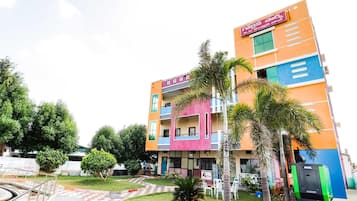 A multi-story building with a colorful facade, a visible signboard, and a paved entrance area with a small garden.