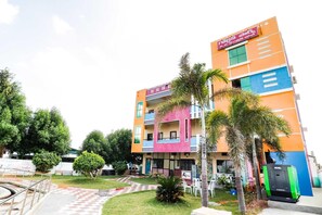 A multi-story building with a colorful facade, a visible signboard, and a paved entrance area with a small garden. - Townhouse CMR Complex Poddatur (Proddatur)