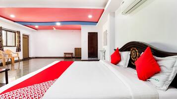 A hotel room with a bed, a red and white patterned runner, a wooden headboard, and a ceiling fan.