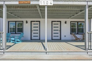 Ein Strandhaus mit zwei Türen, die mit A und B gekennzeichnet sind, einer überdachten Veranda mit blauen Adirondack-Stühlen und einem Schild mit der Aufschrift 'Elvi's Beach House' und der Nummer 1104.