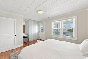 Een slaapkamer met een bed, een deur, een raam met zonwering en een plafondlamp.