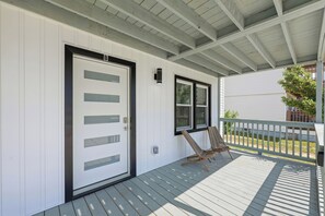 A covered porch with a white door, a window, and two wooden chairs. - Elvi's Beach B | 3BR Coastal Getaway (North Myrtle Beach)