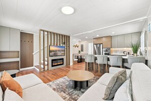 Una sala de estar moderna con chimenea, una zona de comedor y una cocina con electrodomésticos de acero inoxidable.