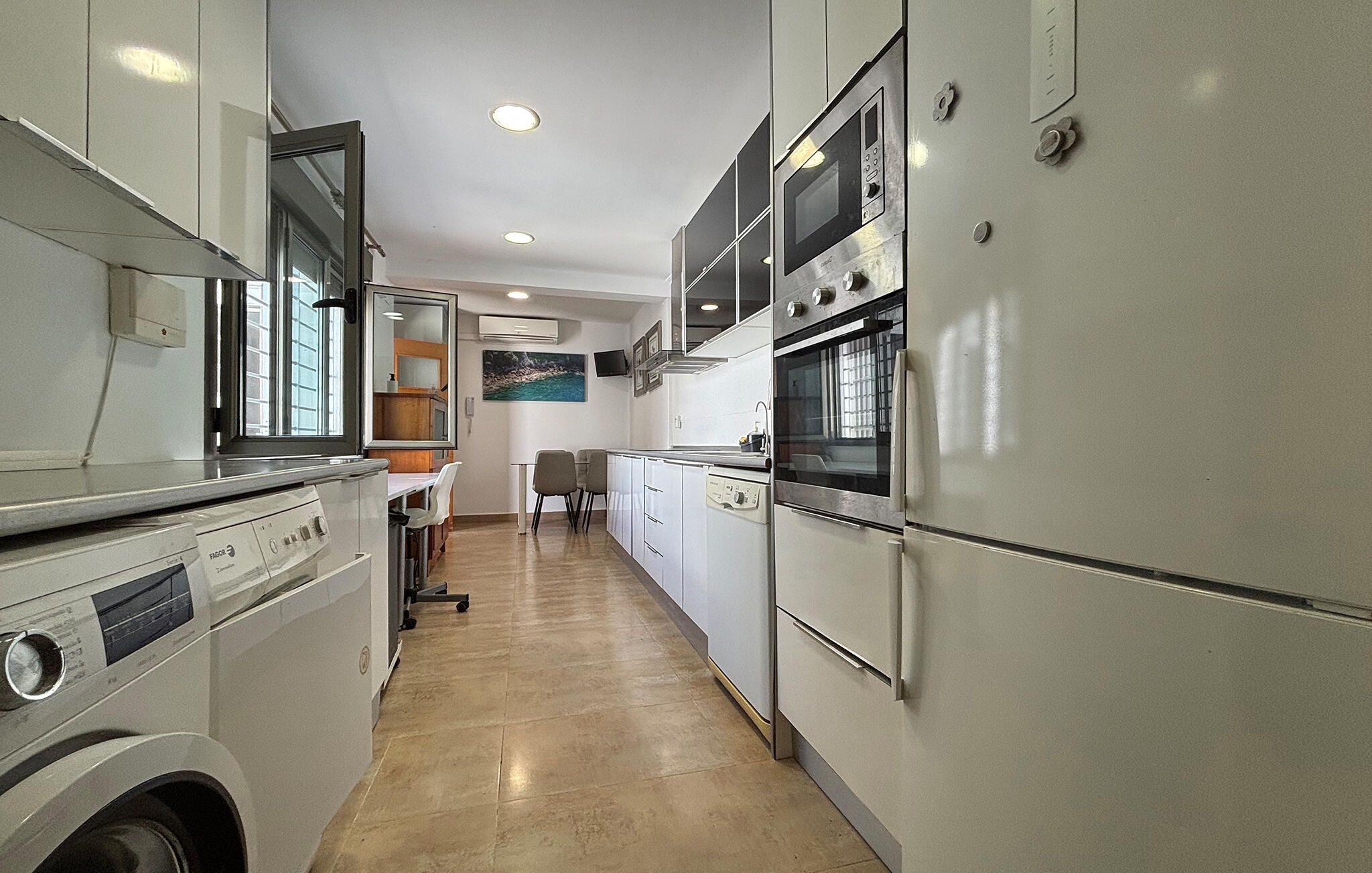 A compact kitchen with a washing machine, a dining area with chairs, and a painting on the wall.