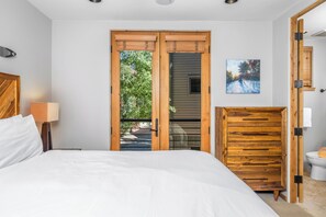 Un dormitorio con cama, un armario de madera, un cuadro y vistas del exterior a través de una puerta.