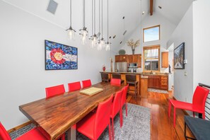 A dining area with a wooden table and red chairs, a kitchen with wooden cabinets, and a large abstract painting on the wall. - New! Ski Days + Sunset Après | 3BR Mountain Retreat | Walk to Ski + Garage (Telluride)