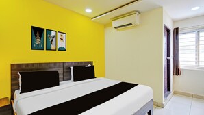 Quarto de hotel com cama, cabeceira, ar condicionado fixado na parede e janela com cortinas.