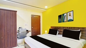 Quarto de hotel com cama, guarda-roupa, secretária e chaleira, além de uma porta.