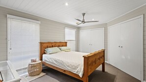 Une chambre à coucher avec un lit en bois, un ventilateur de plafond et des armoires blanches.