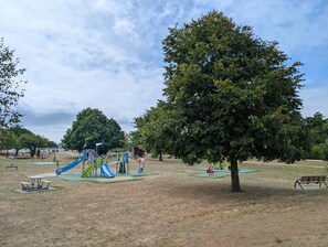 A park with playground equipment, picnic tables, and a large tree. - Le Refuge de Césarine - CARNAC (CARNAC)