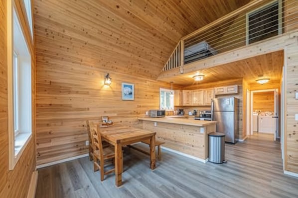 A wooden interior with a dining table, kitchen area, and a staircase. - Gorgeous 2-bedroom cabin in charming Big Lake perfect for relaxing getaway (Big Lake)