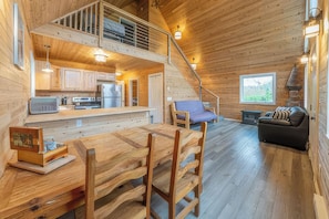 A wooden cabin interior with a dining area, kitchen, and a staircase leading to an upper level. - Gorgeous 2-bedroom cabin in charming Big Lake perfect for relaxing getaway (Big Lake)