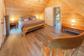 A wooden room with a bed, bedside table, and a chair.