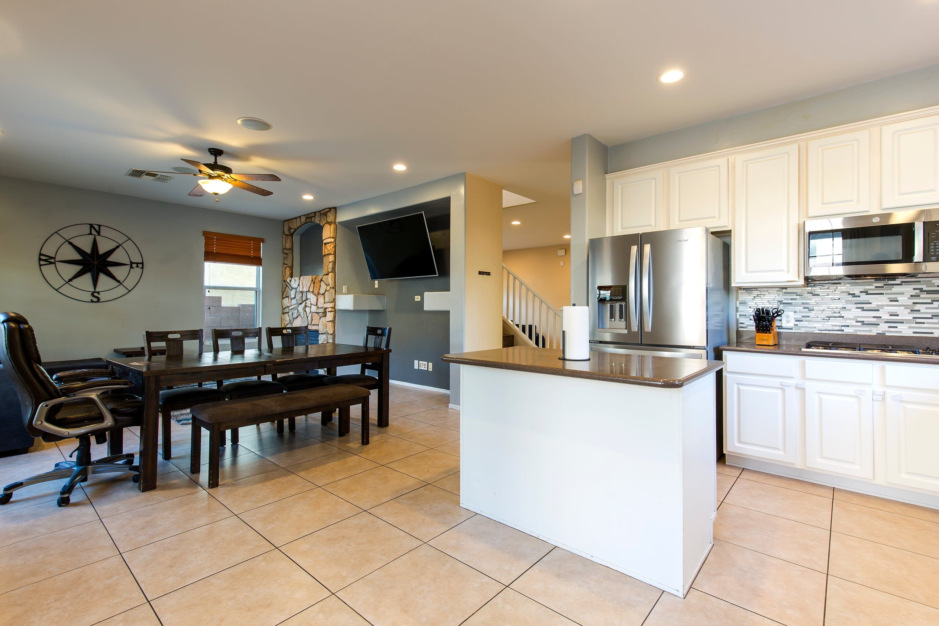 A modern kitchen with white cabinetry, a stainless steel refrigerator, and a flat-screen TV mounted on the wall.