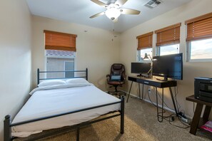 Un dormitorio con cama, escritorio con computadora, silla y ventilador de techo.