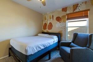 A bedroom with a single bed, a chair, and a window with blinds. - The Lindenthal | Family Friendly 5BR | Fenced Yard | Sleeps 10 (Tucson)