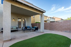 Un patio techado con mobiliario exterior y una pequeña sección de césped artificial.
