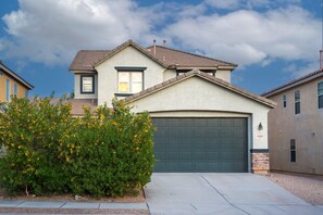 A two-story house with a green garage door, a small attached garage, and a clear sky with clouds. - The Lindenthal | Family Friendly 5BR | Fenced Yard | Sleeps 10 (Tucson)