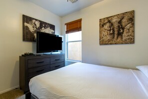 A bedroom with a bed, a TV on a dresser, and two large paintings on the walls. - The Lindenthal | Family Friendly 5BR | Fenced Yard | Sleeps 10 (Tucson)