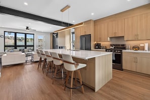 A modern kitchen with a central island, bar stools, a refrigerator, stove, and a view of a residential area. - Newly Built Modern Townhome - Pet Friendly, Private Hot Tub, Walk to Restaurants (Fraser)