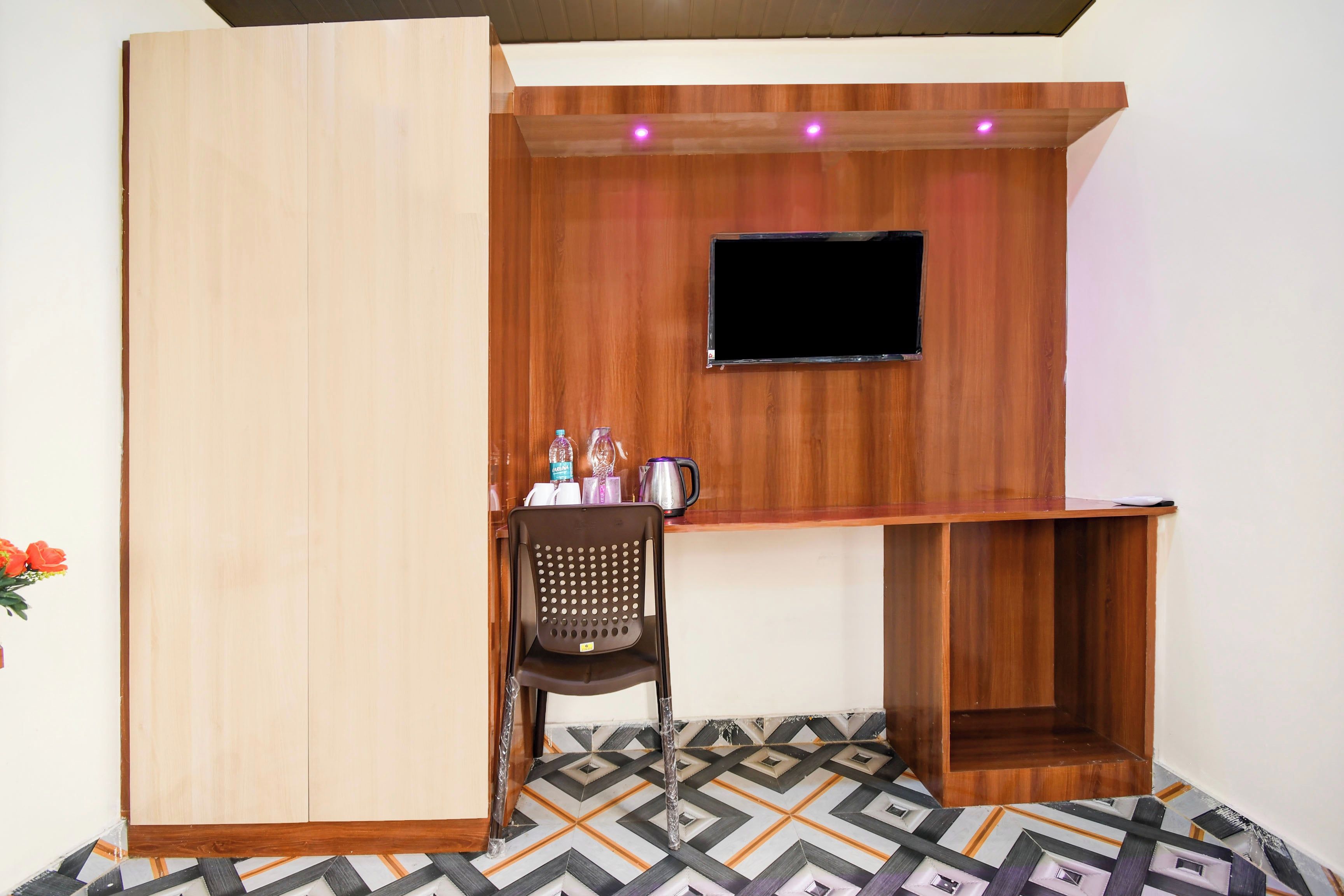 A room with a wooden TV stand, a small seating area, and a patterned floor.