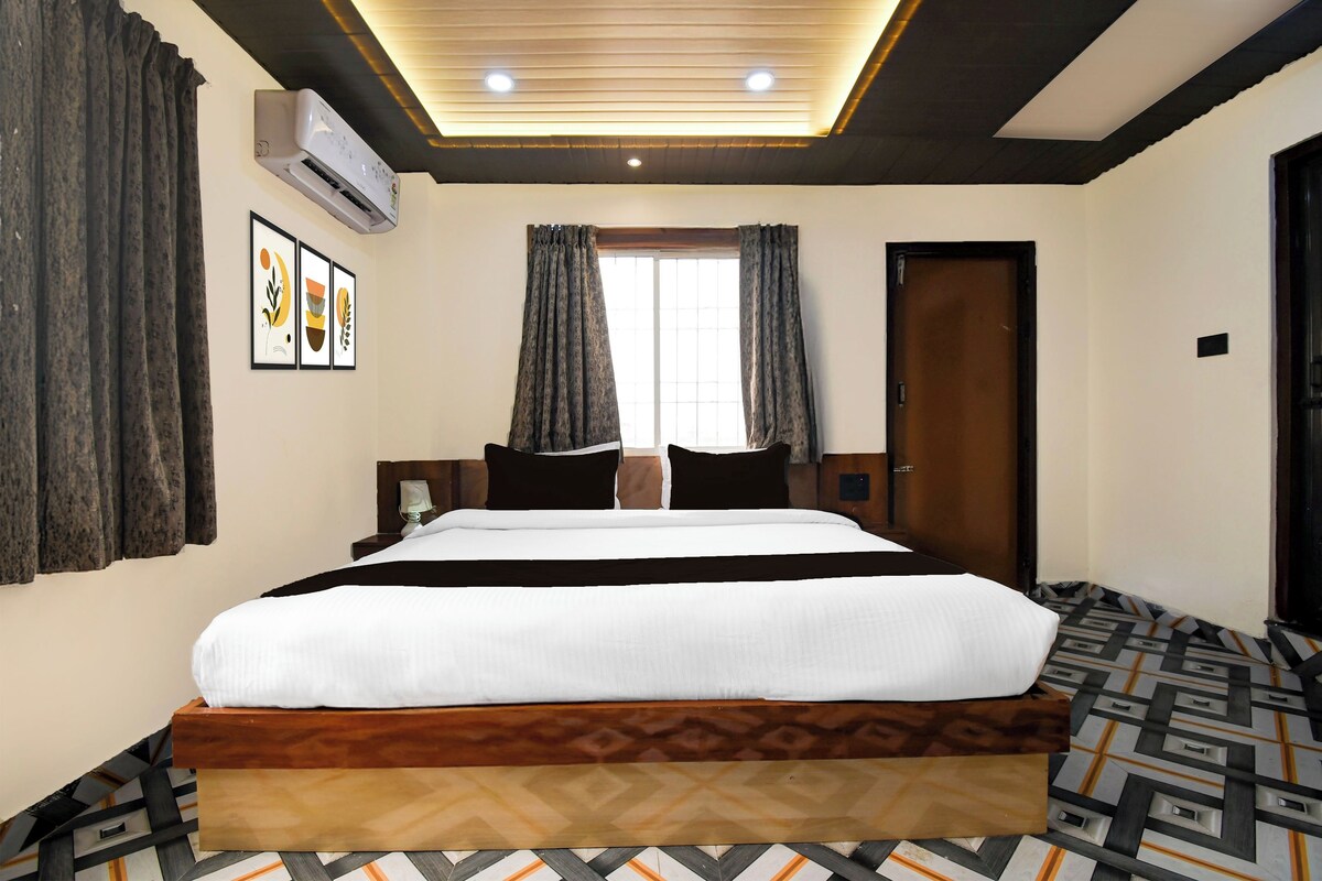 Una habitación de hotel con una cama grande, una mesita de noche, una lámpara, una ventana con cortinas, un equipo de aire acondicionado y un piso con diseño.