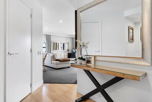 A modern interior with a minimalist design, featuring a white sofa, a glass-top console table, and a large mirror. - Rare 2 Bed 2 Bath Corner Apartment at Latitude 37 (Auckland City)
