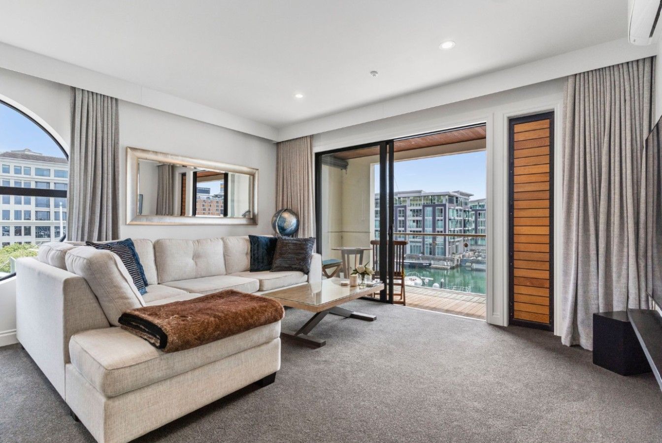A modern hotel room with a sofa, a coffee table, and a view of a cityscape through large windows.