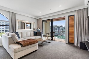 A modern hotel room with a sofa, a coffee table, and a view of a cityscape through large windows. - Rare 2 Bed 2 Bath Corner Apartment at Latitude 37 (Auckland City)