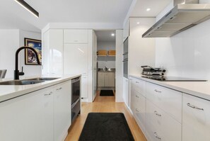 A modern kitchen with white cabinetry, stainless steel appliances, and a black rug on the floor. - Rare 2 Bed 2 Bath Corner Apartment at Latitude 37 (Auckland City)