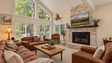 A spacious living room with leather sofas, a fireplace, and large windows.