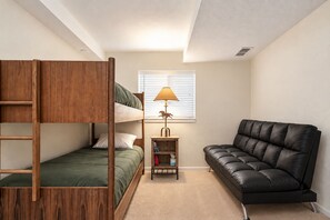 A room with a bunk bed, a desk with a lamp, and a leather sofa.