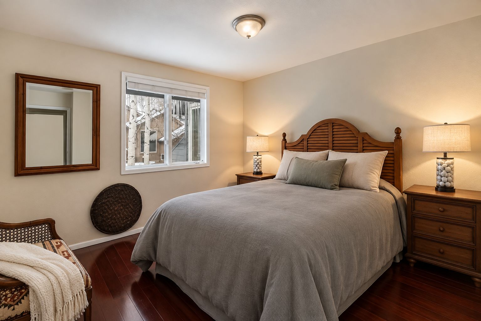 A bedroom with a large bed, two bedside tables with lamps, a mirror, and a window with a view of buildings.