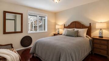 A bedroom with a large bed, two bedside tables with lamps, a mirror, and a window with a view of buildings.