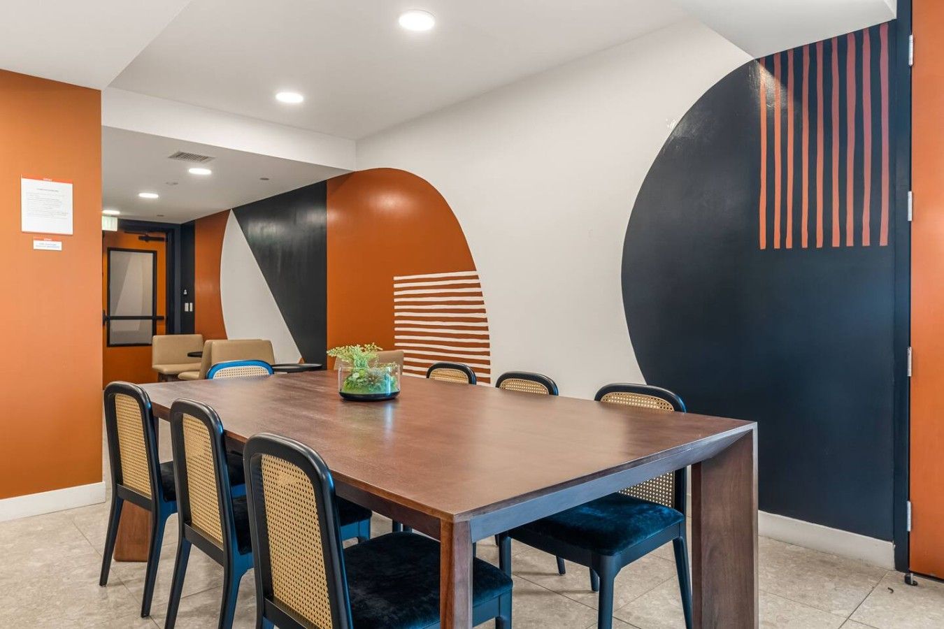 Un salón de conferencias con una larga mesa, sillas y un centro de mesa con planta decorativa.