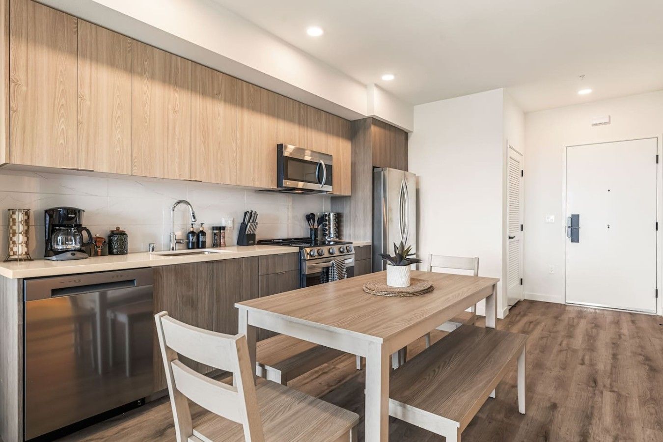 A modern kitchen with wooden cabinets, stainless steel appliances, and a dining area with a wooden table and chairs.