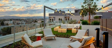 A rooftop terrace with outdoor seating, a fire pit, and a view of the cityscape.