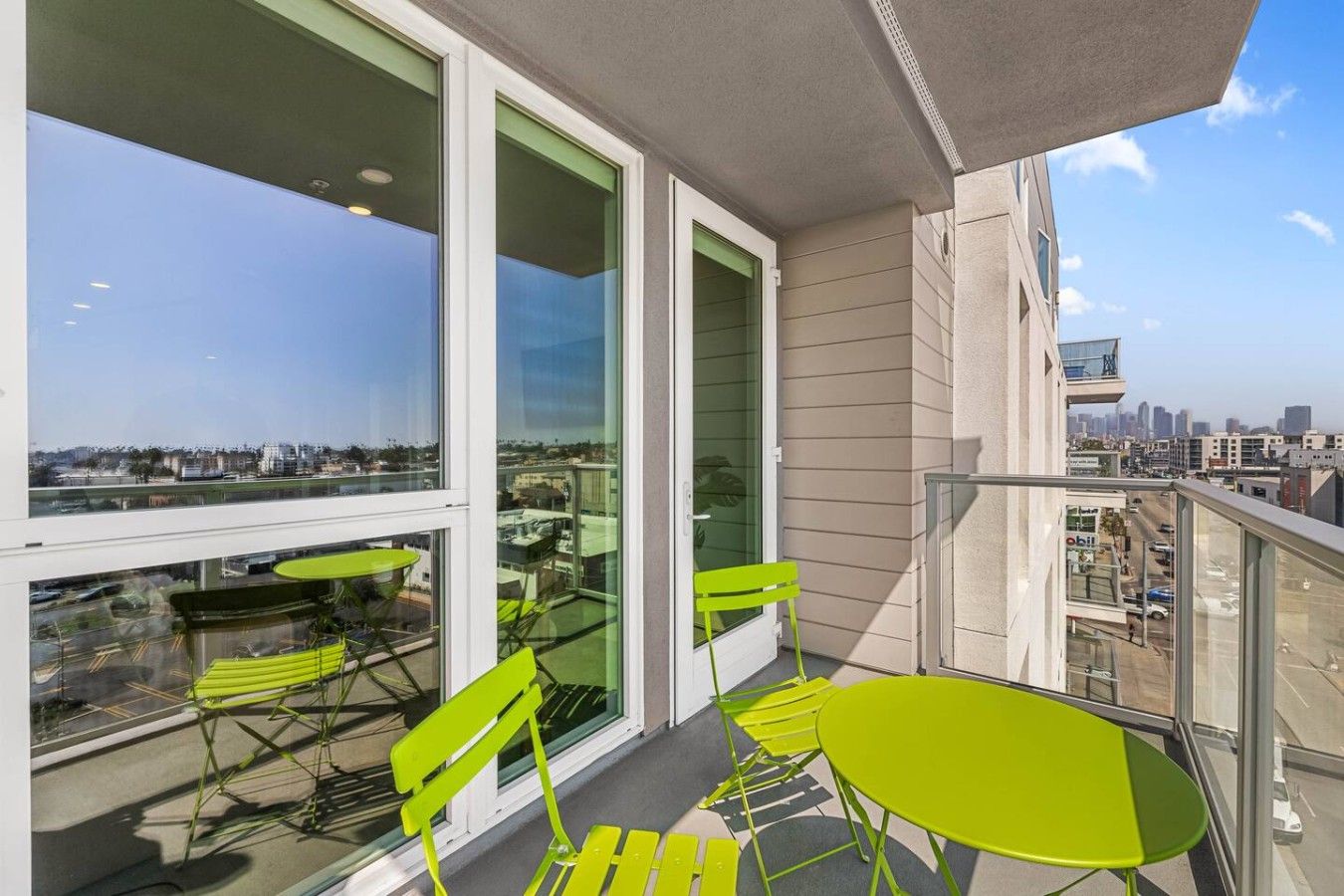 Un balcón con mesa y sillas, ventanas amplias y vistas de la ciudad.