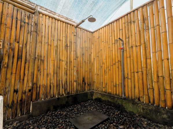 A traditional Japanese onsen with bamboo walls, a stone hot spring, and a showerhead.
