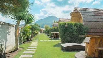 Un sendero conduce a un edificio con techo tradicional, rodeado de abundante vegetación y una montaña al fondo.