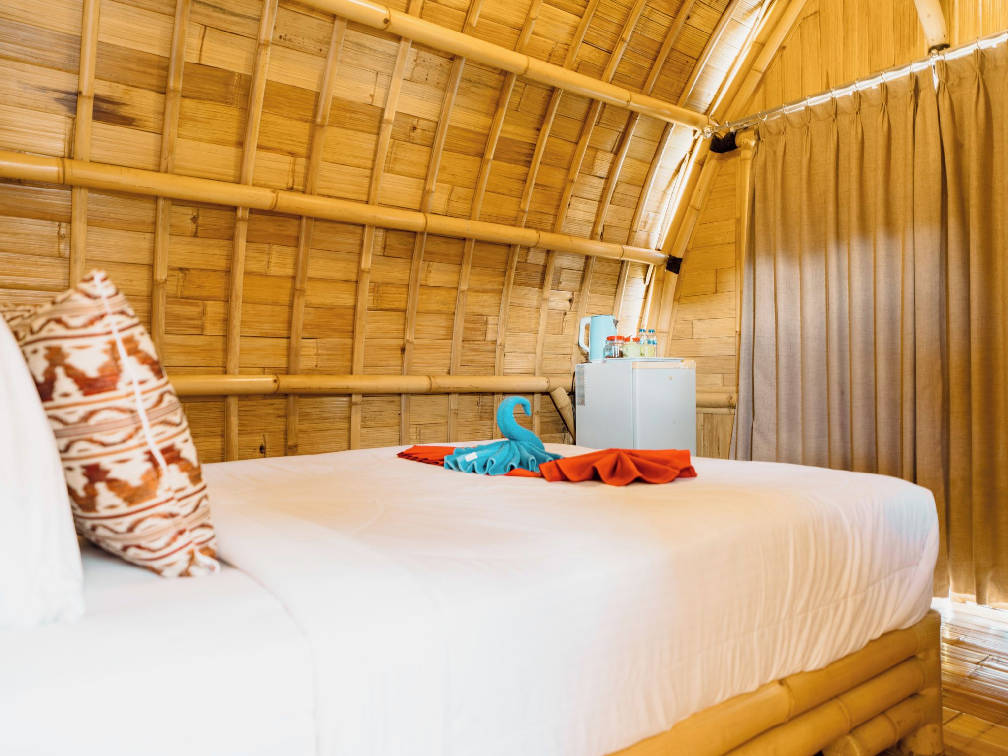 Una habitación con cama, almohada, toalla, una mesita y una ventana con cortinas.