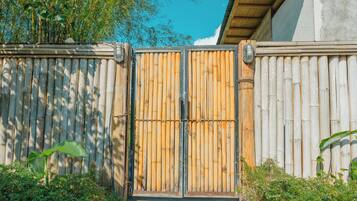 A bamboo fence with a metal gate, surrounded by greenery and a clear sky.