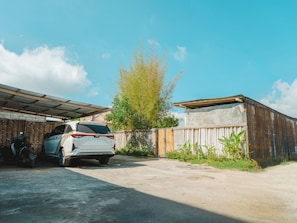 A white SUV parked in a driveway with a motorcycle beside it, a wooden fence, and a tree in the background.