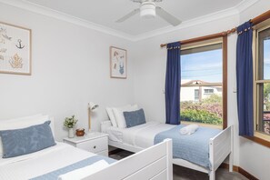 Une chambre avec deux lits, une table de chevet, une lampe et une fenêtre avec des rideaux.